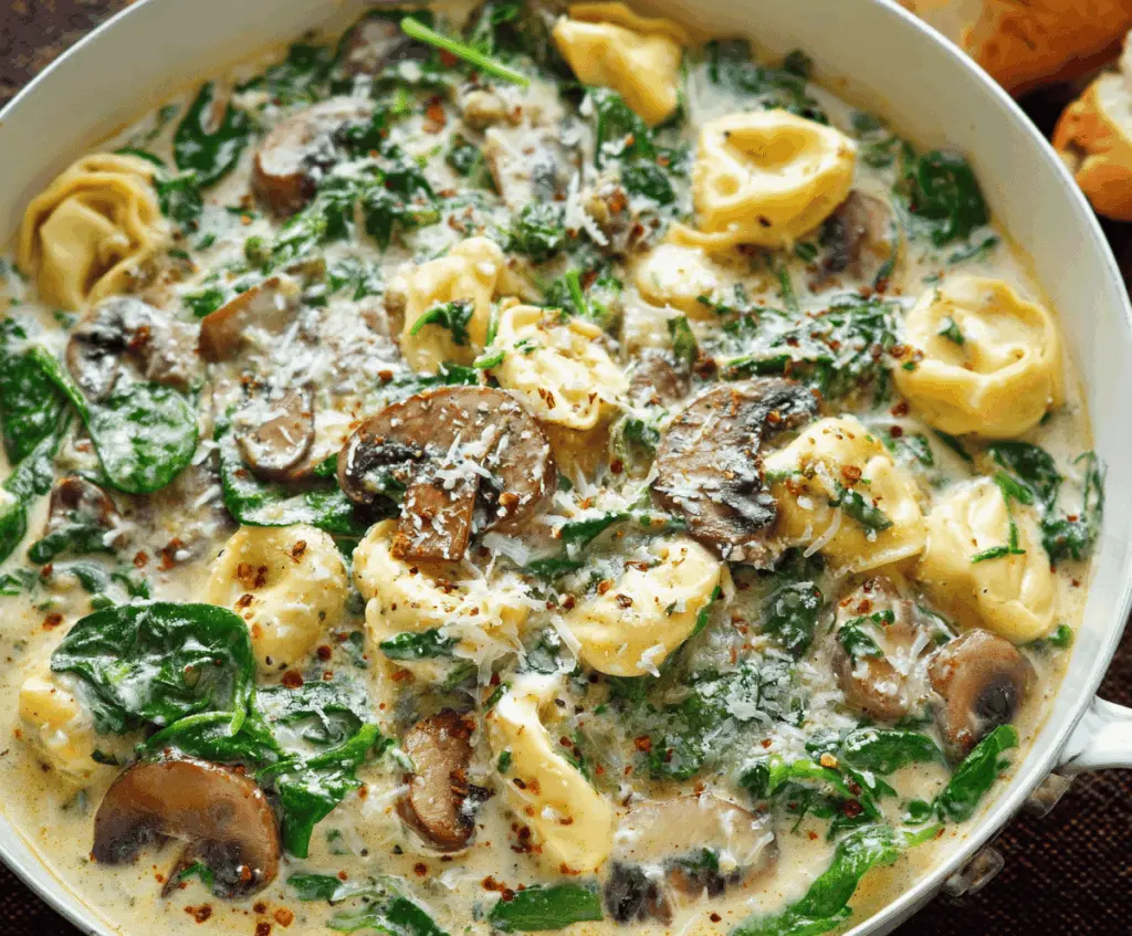 Creamy tortellini pasta with fresh spinach and sautéed mushrooms served in a bowl, delicious Italian-inspired dish