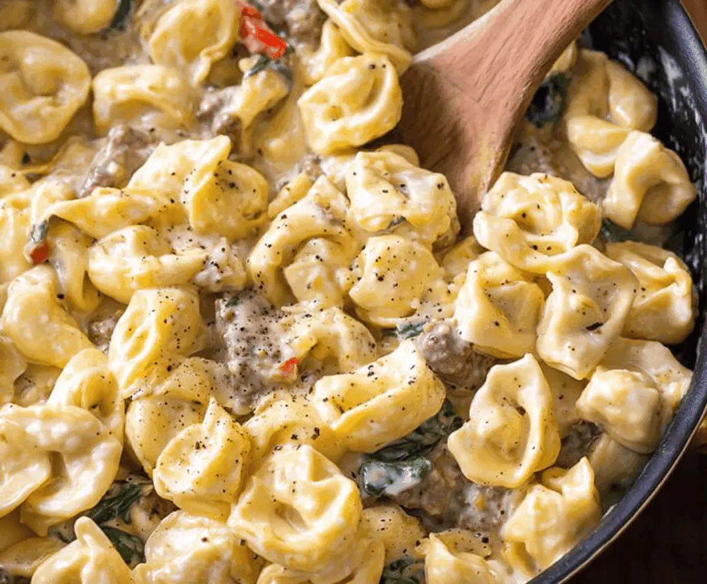 Creamy garlic butter beef and spinach tortellini dish with melted cheese and fresh herbs on a white plate