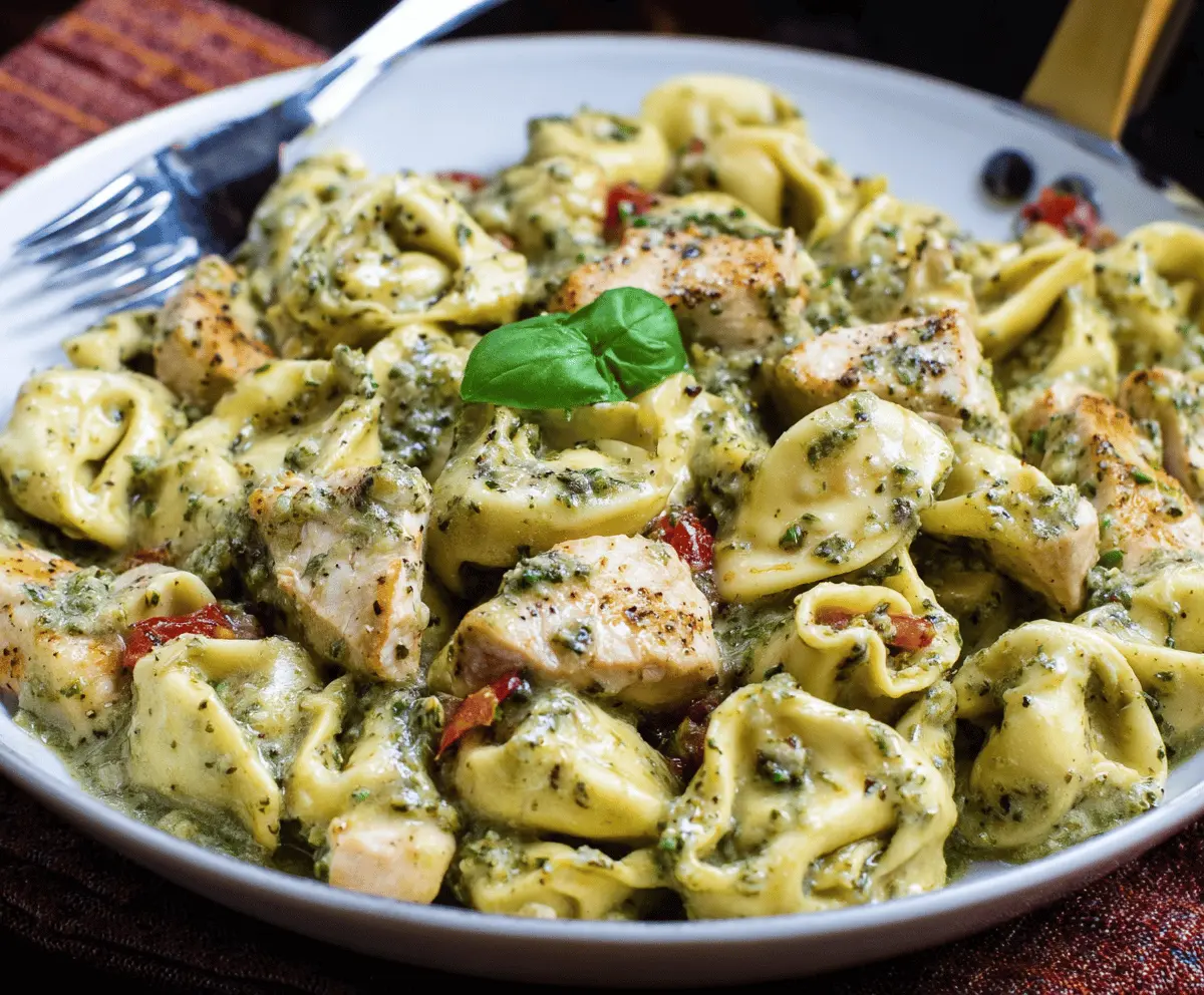 Creamy pesto chicken tortellini served on a white plate topped with fresh basil and grated Parmesan cheese, garnished with cherry tomatoes and herbs.